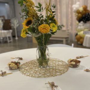 Center piece created with an arrangement of yellow flowers in a vase sits on a table with small bowls containing a snack mix and a small gift left at each guests place at the table.